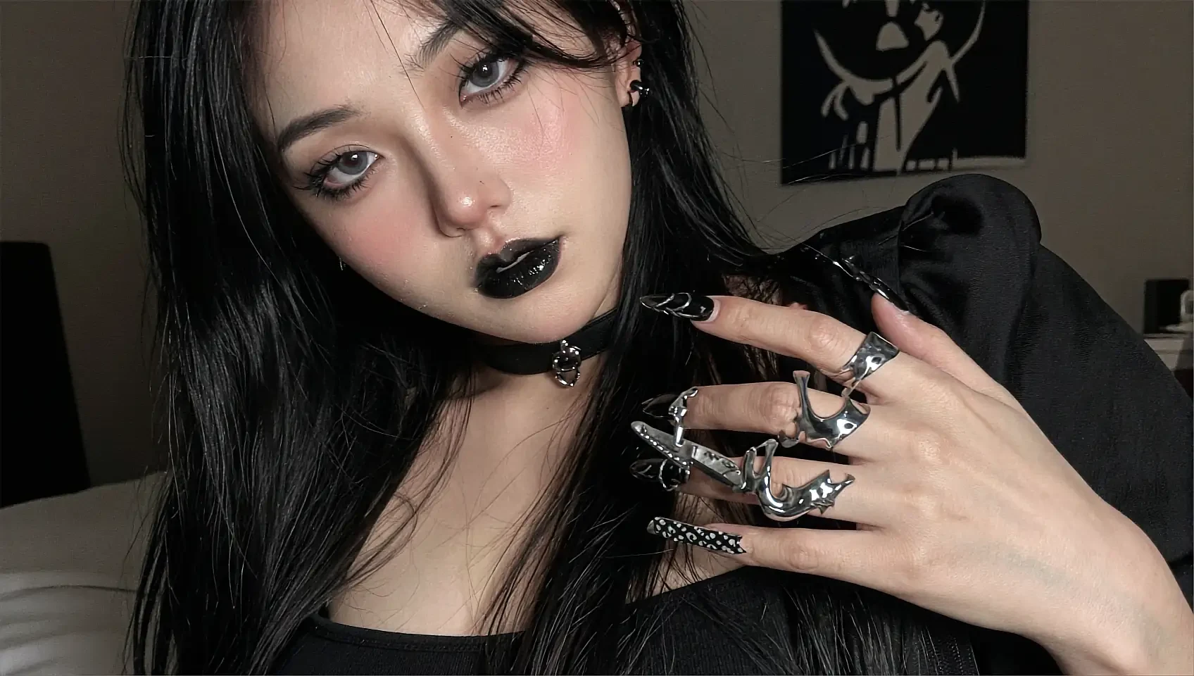 Woman with dark eye make-up and black nail varnish lying on a bed in a dim room